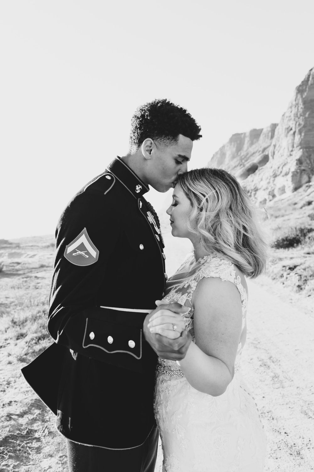 A black and white close-up captures a tender moment between newlyweds against rocky cliffs.
