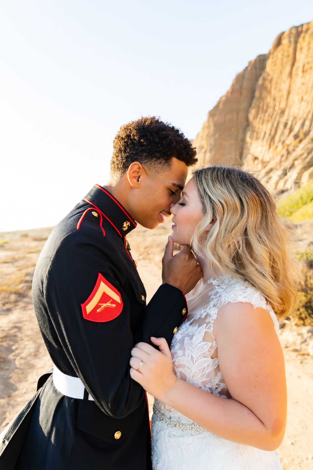 Intimate portrait of military couple in dress blues and wedding gown against desert backdrop.