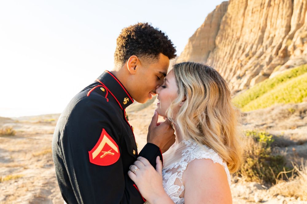 Close up romantic moment of military couple in dress blues and wedding dress with desert background.