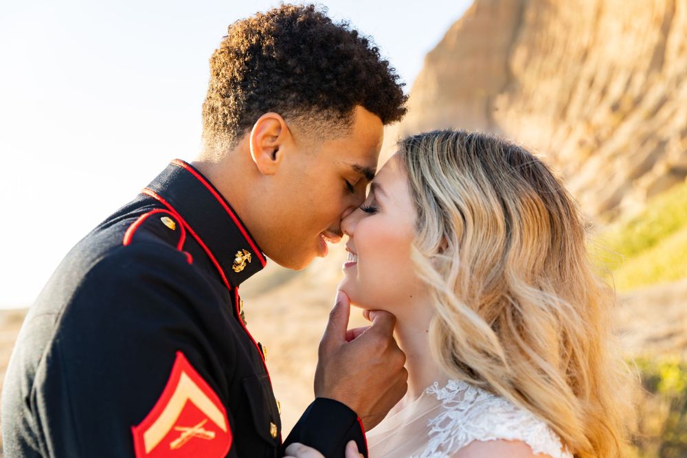 Marine in dress uniform and bride share a tender moment during their wedding photoshoot by cliffs.