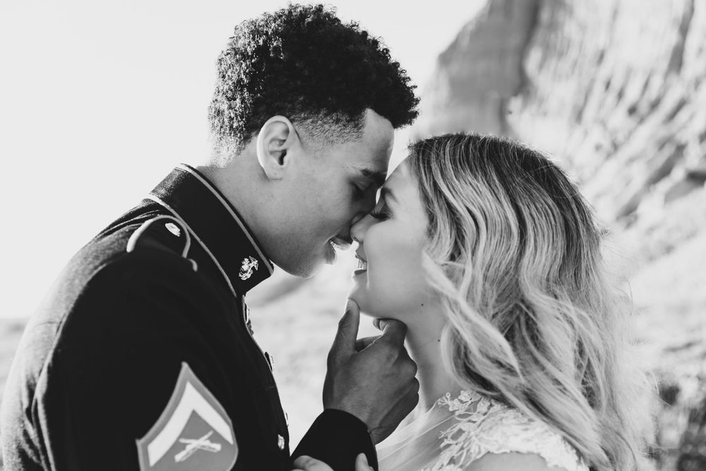 A romantic black and white portrait of a Marine and bride sharing an intimate moment against a rocky backdrop.