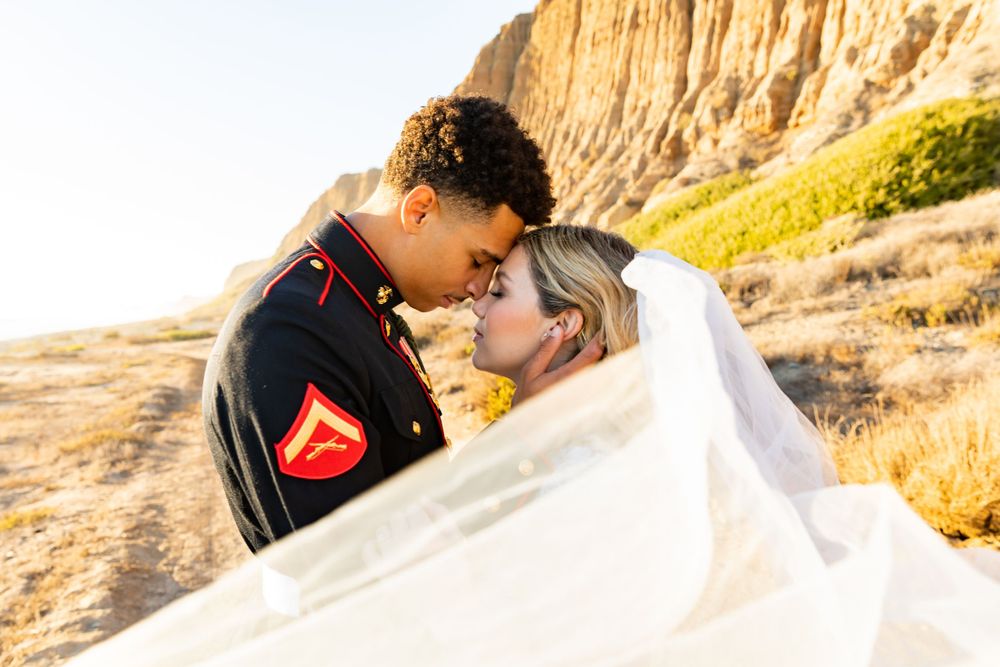 Artistic wedding photo with flowing white veil as couple shares romantic moment by cliffs.