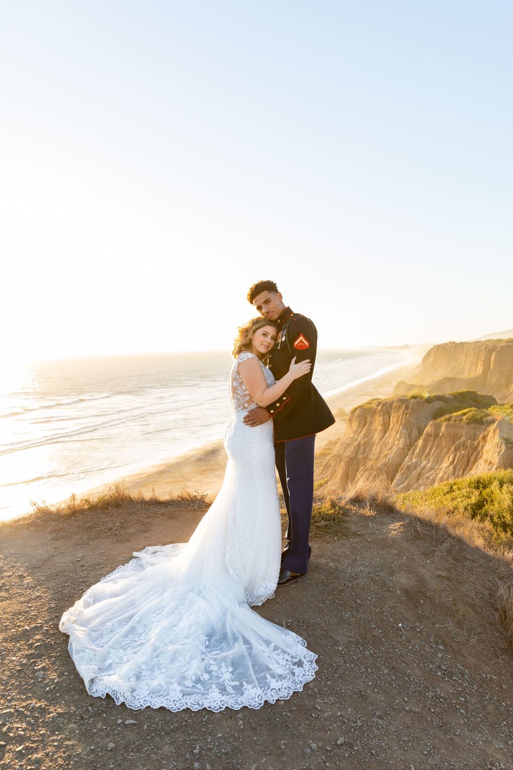 Newlyweds share an intimate moment on oceanside cliffs during golden hour sunset.