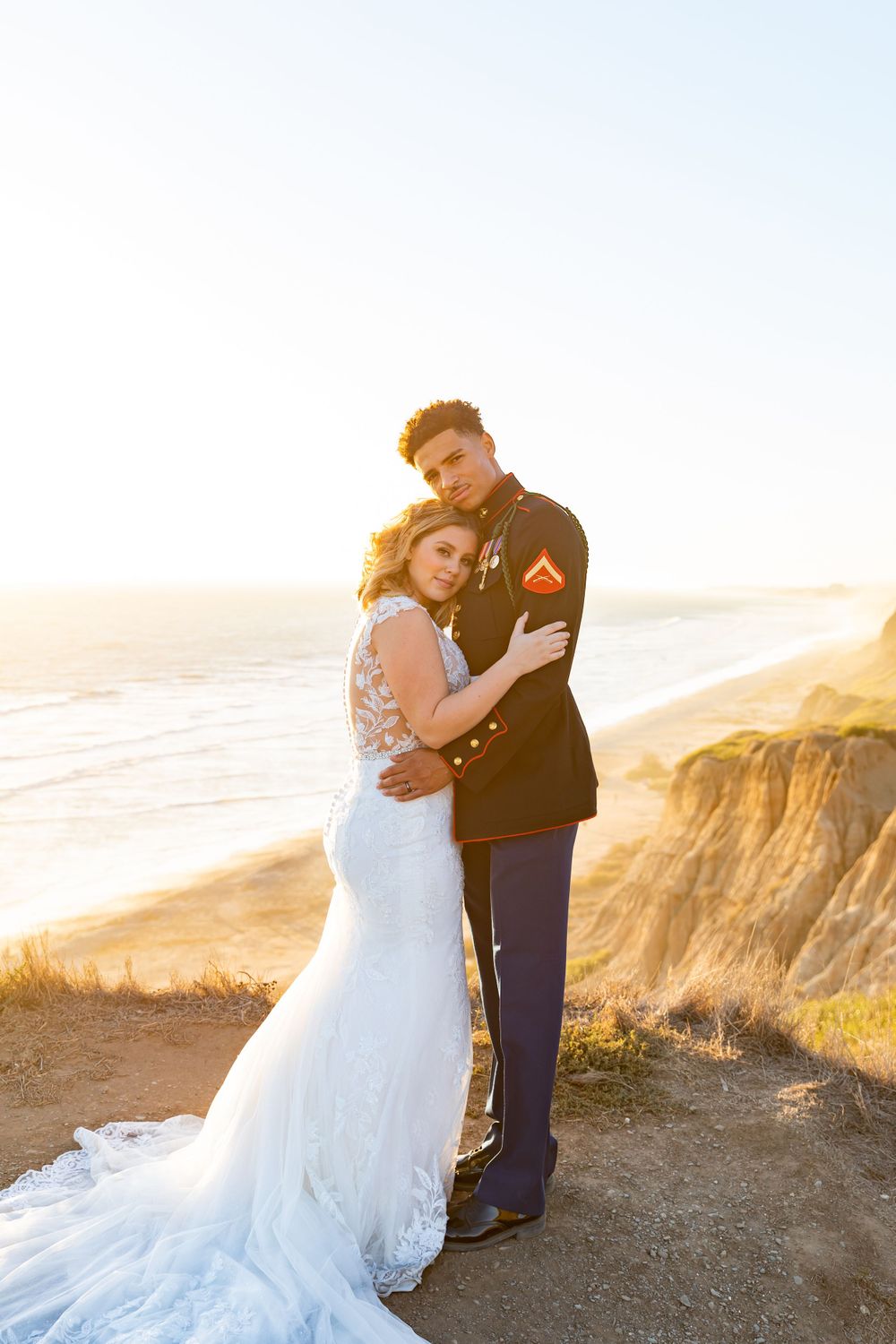 A romantic wedding portrait captured against dramatic coastal cliffs at sunset.