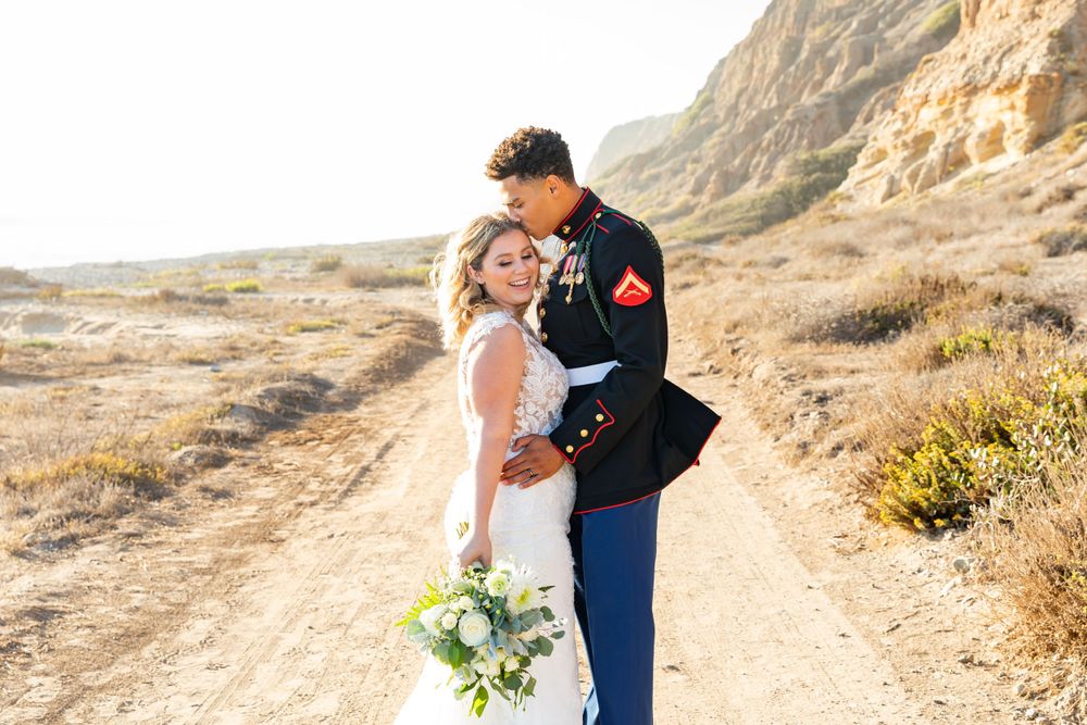 A joyful wedding couple shares a romantic moment on a desert trail with cliffs in the distance.