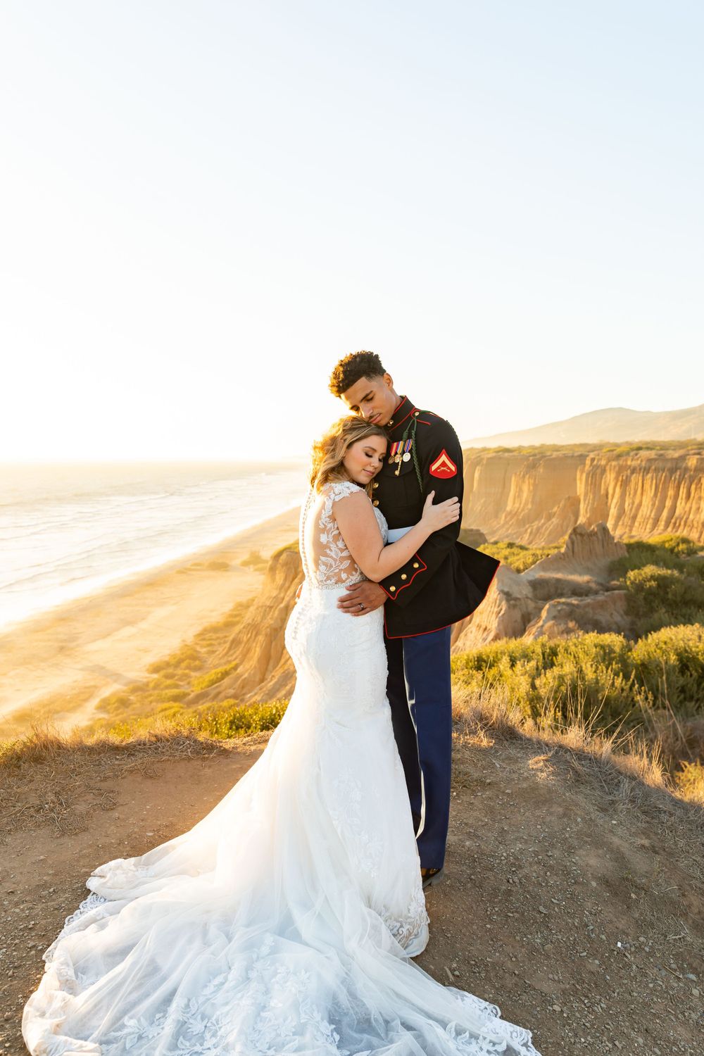 Sunset wedding photo of couple embracing on dramatic coastal cliffs with long train dress.
