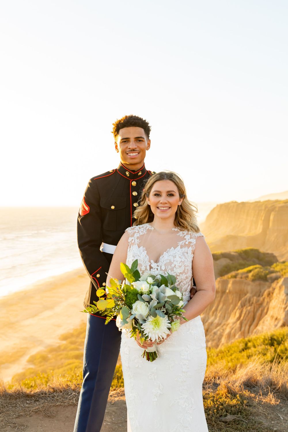 Military wedding couple poses with bridal bouquet on scenic coastal overlook.