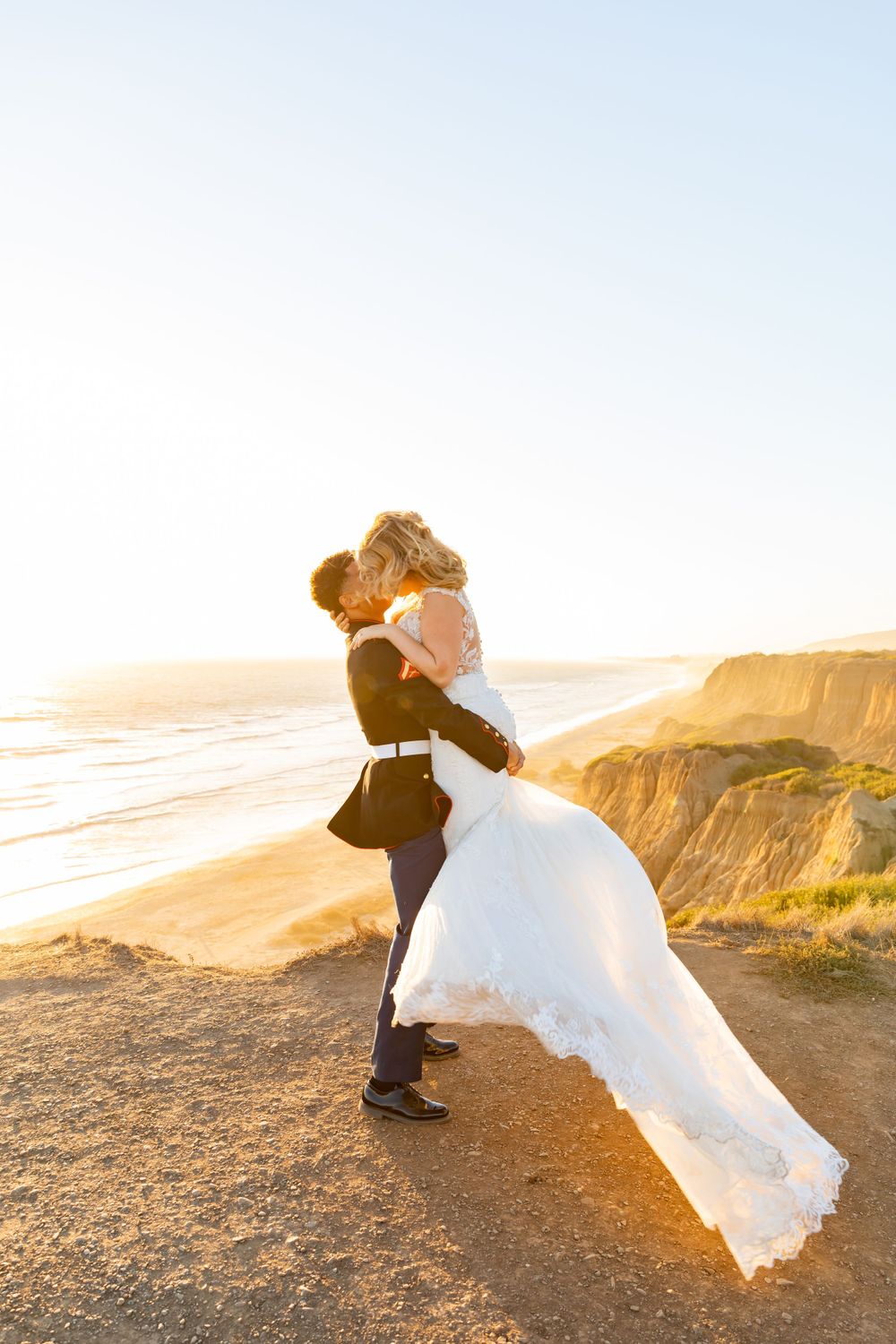 A romantic wedding portrait showing a couple dancing on a cliff overlooking the ocean at sunset.