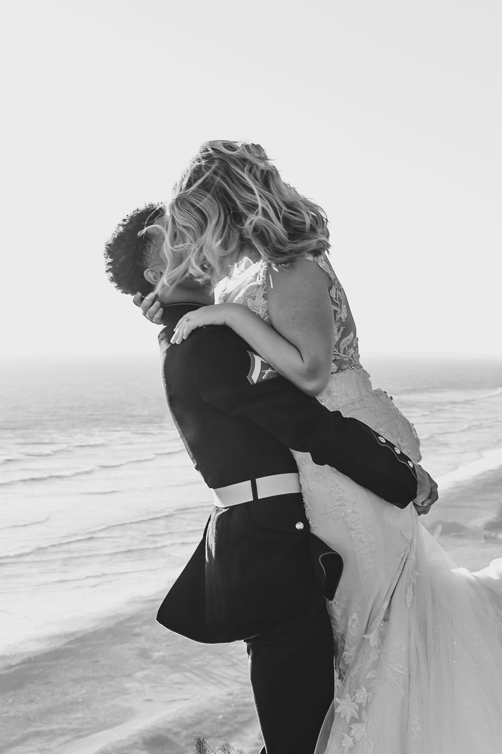 An intimate black and white portrait of newlyweds embracing against a coastal backdrop.