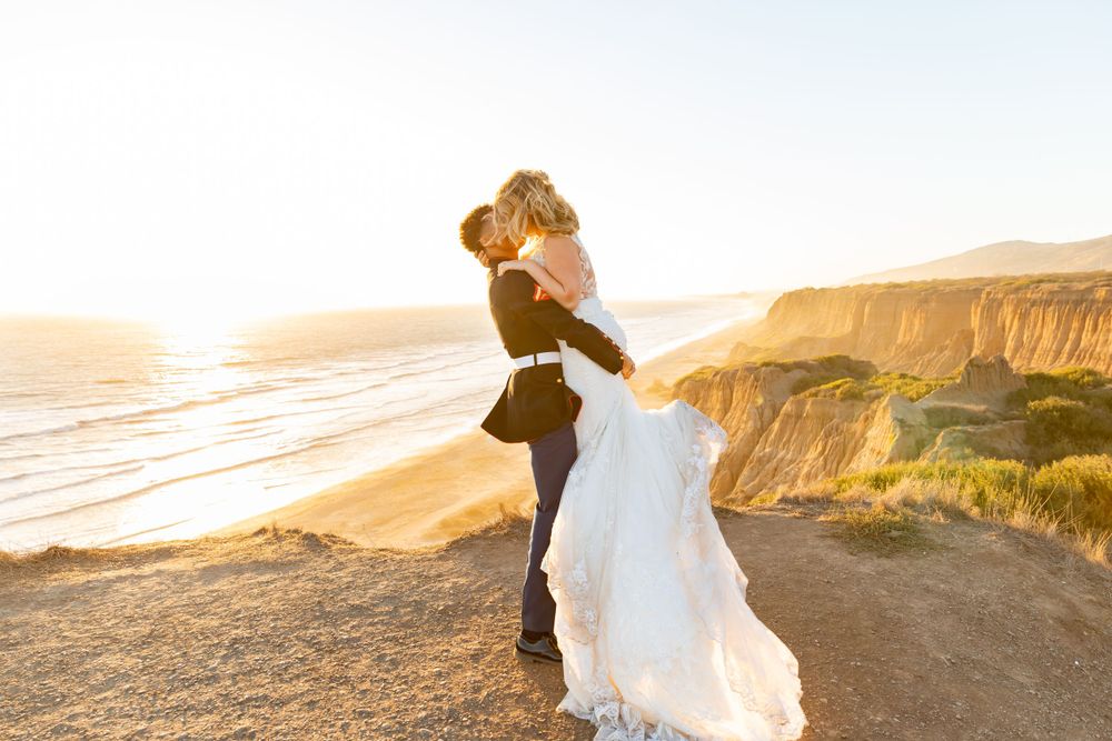 A romantic golden hour portrait of newlyweds sharing a moment on coastal cliffs.