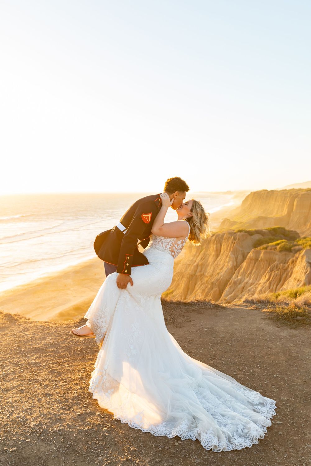 Newlywed couple sharing romantic moment at sunset on coastal cliffs overlooking ocean.