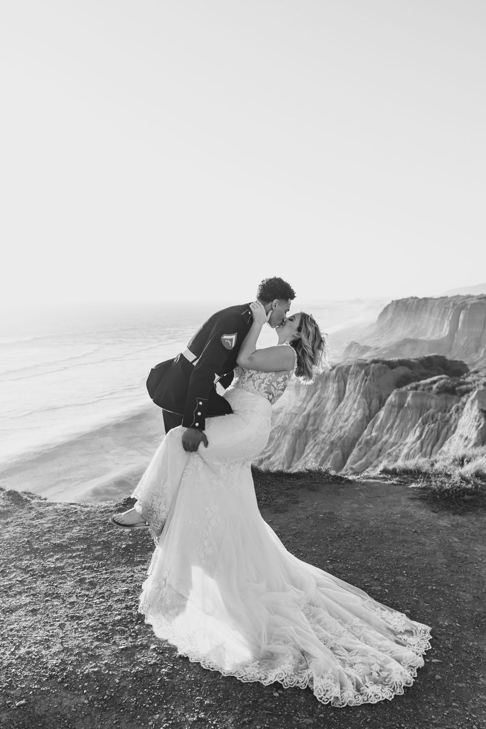 Black and white photo of wedding couple embracing on dramatic coastal cliffs.