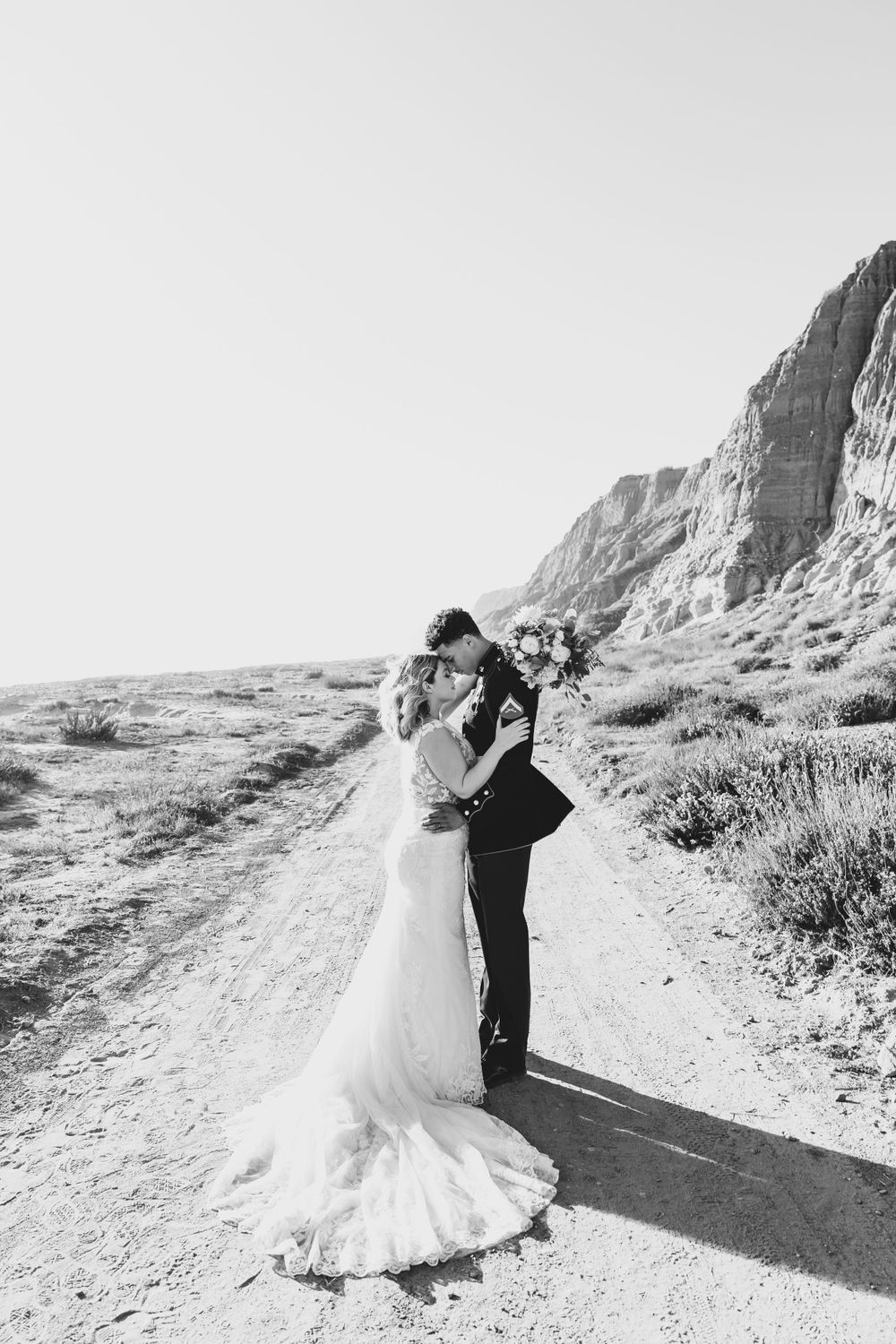 Black and white wedding photo of newlyweds sharing an intimate moment against desert cliffs.