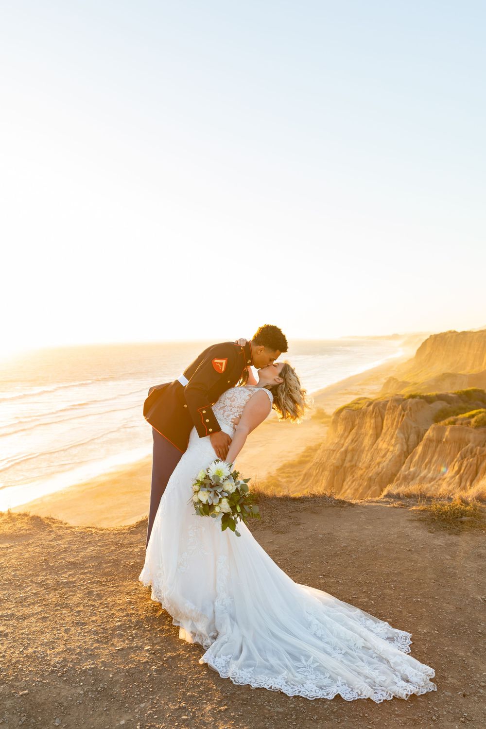 Romantic wedding portrait with flowing lace dress against golden coastal cliffs.