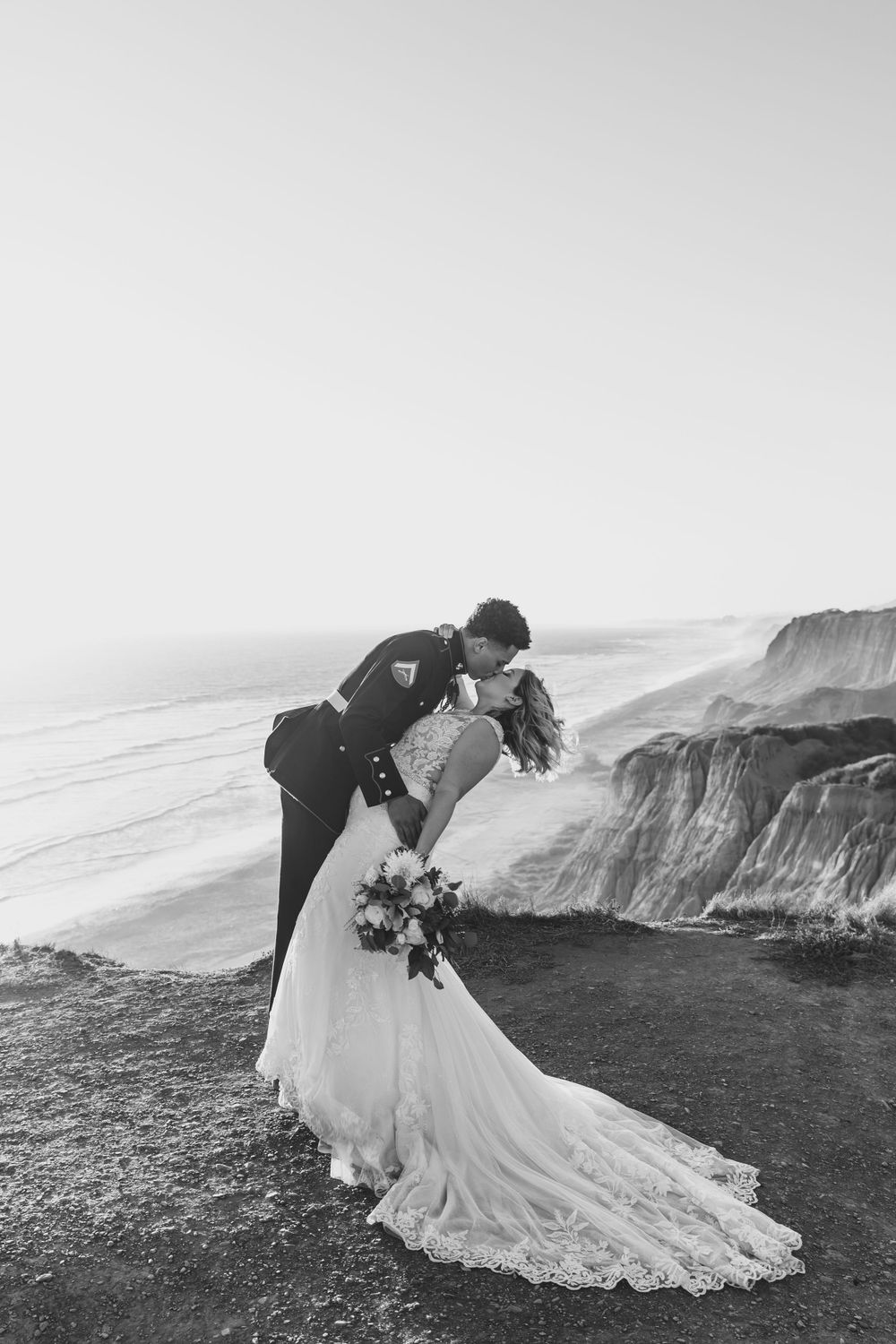 Dramatic black and white wedding photo of couple on clifftop overlooking ocean.