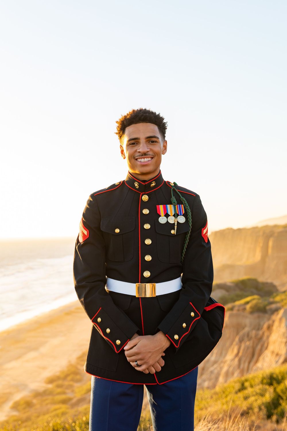 US Marine in dress blues with medals posing on clifftop at golden hour.