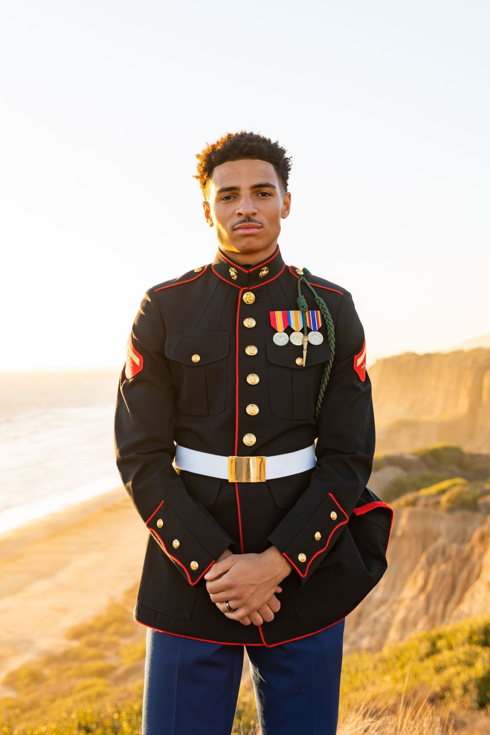 Marine in dress uniform poses against coastal cliffs at golden hour.