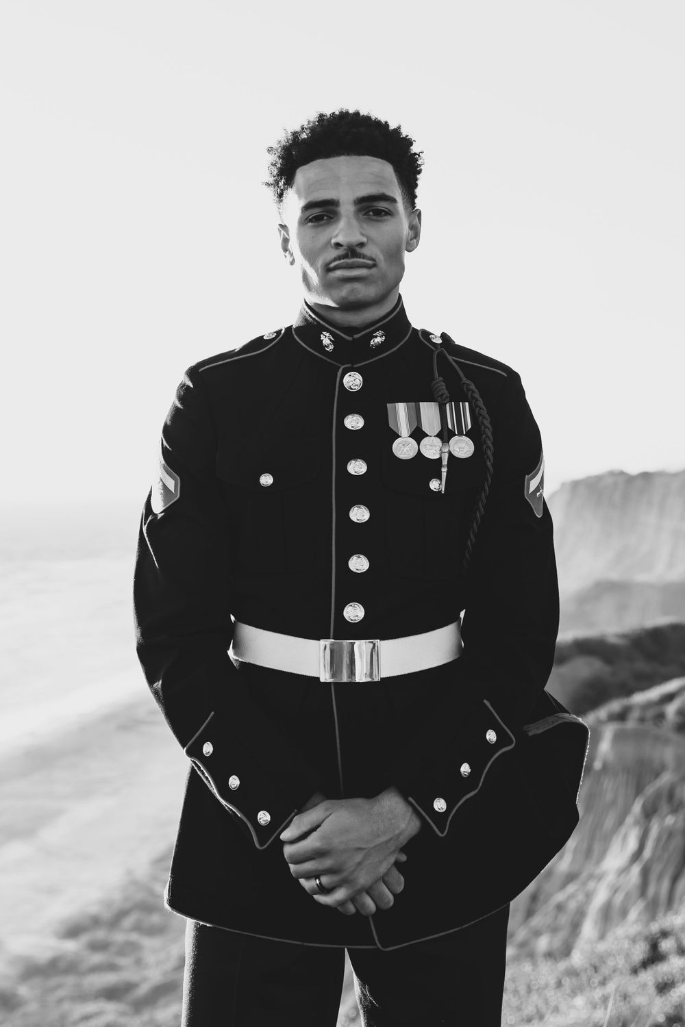 Black and white portrait of Marine in dress uniform with medals against coastal backdrop.