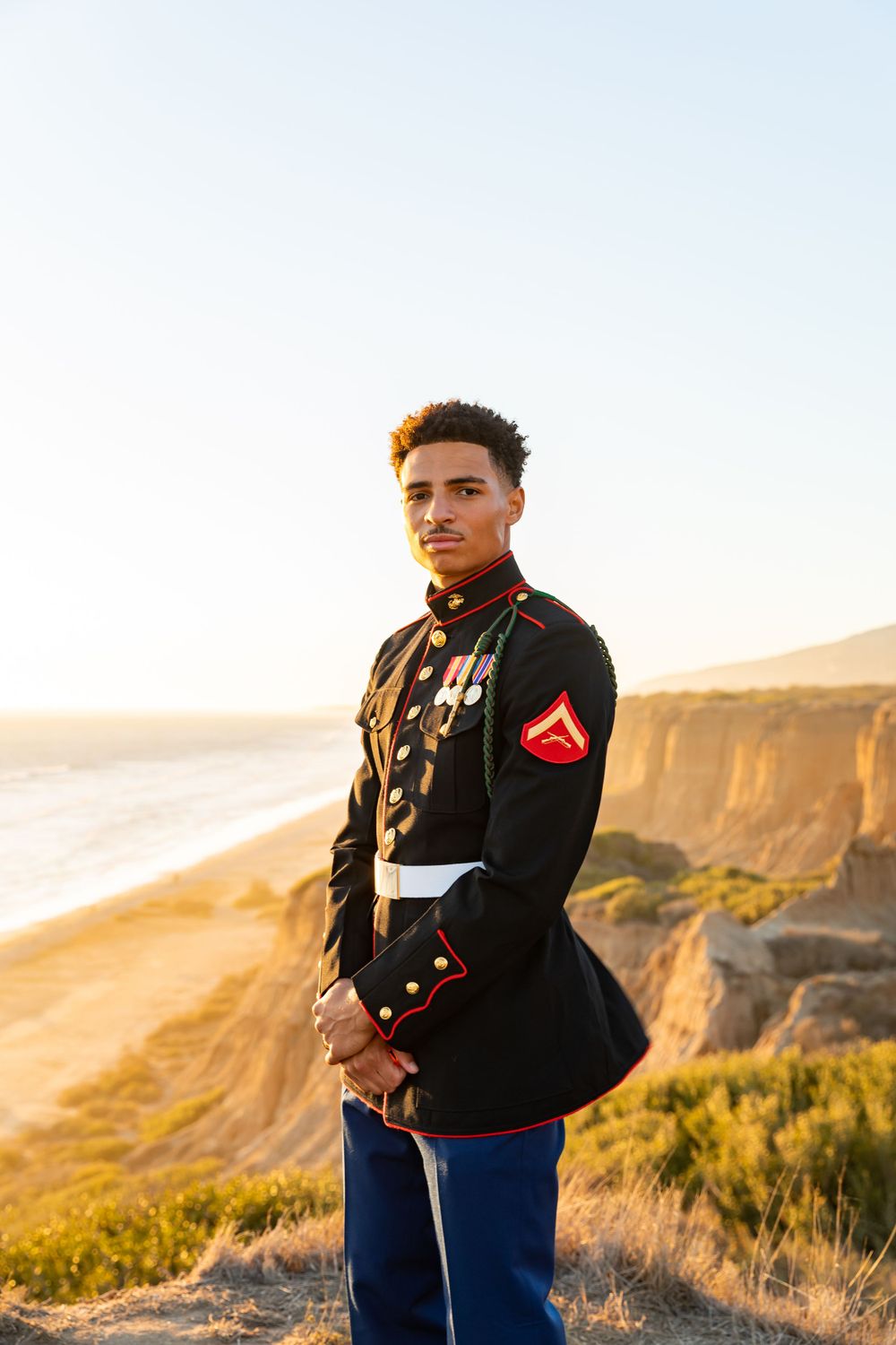 Marine stands proudly in dress blues overlooking scenic ocean cliffs.
