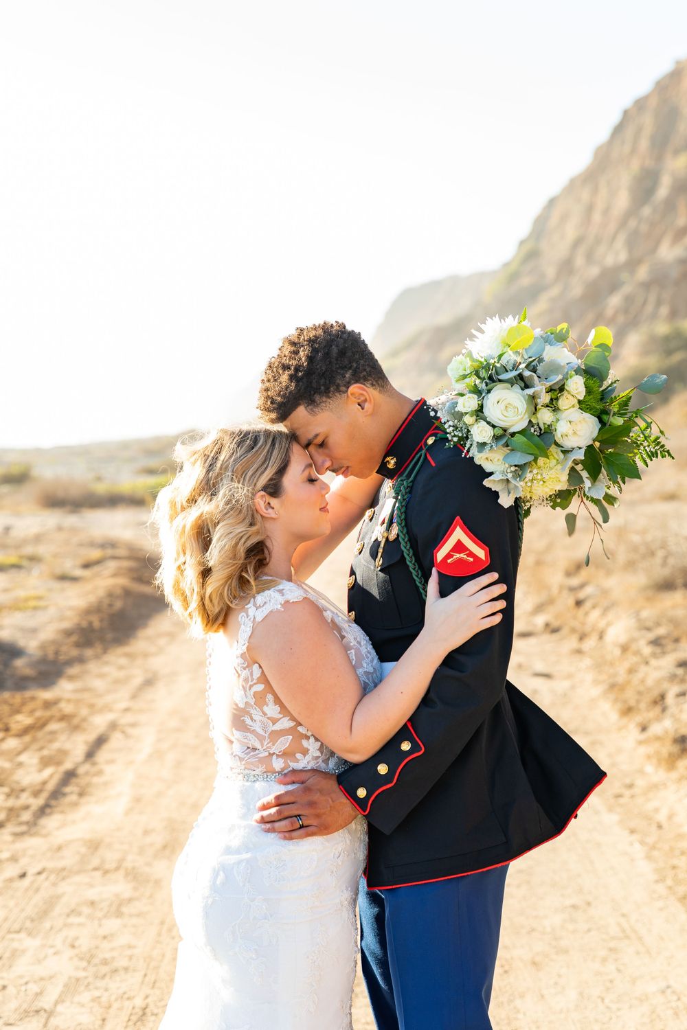 A Marine and bride share a romantic moment with a stunning bouquet and desert landscape.