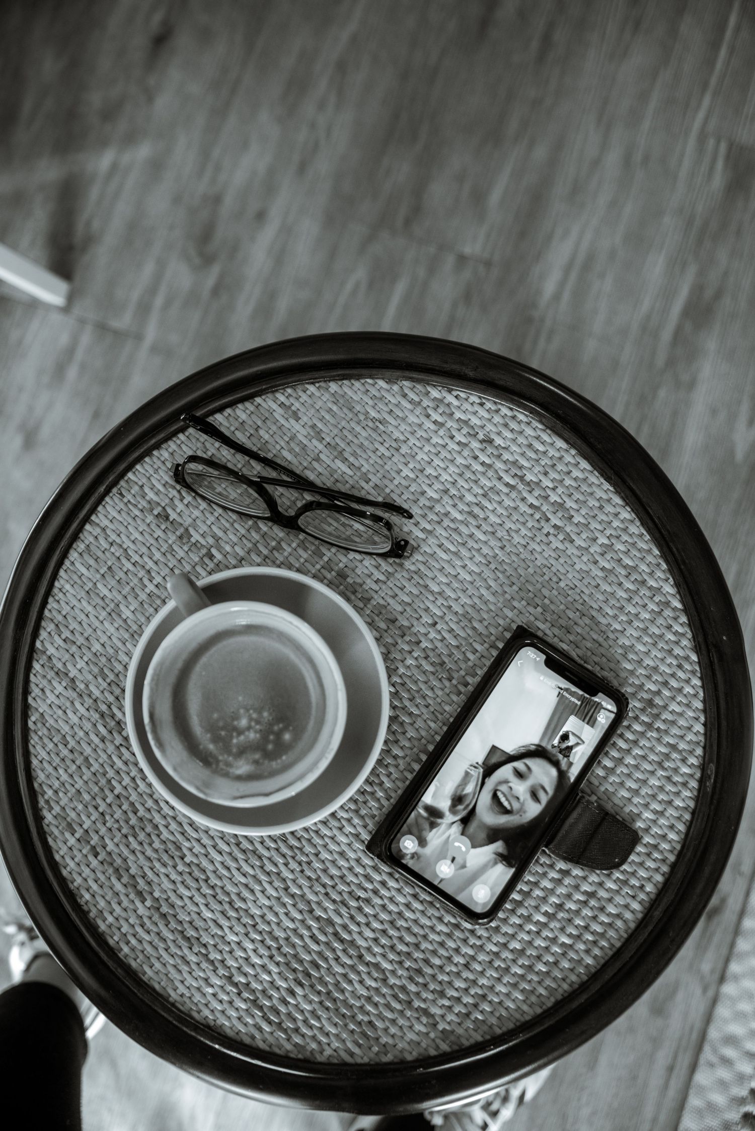 Overhead photo of coffee cup, glasses and phone on textured gray surface in monochrome.