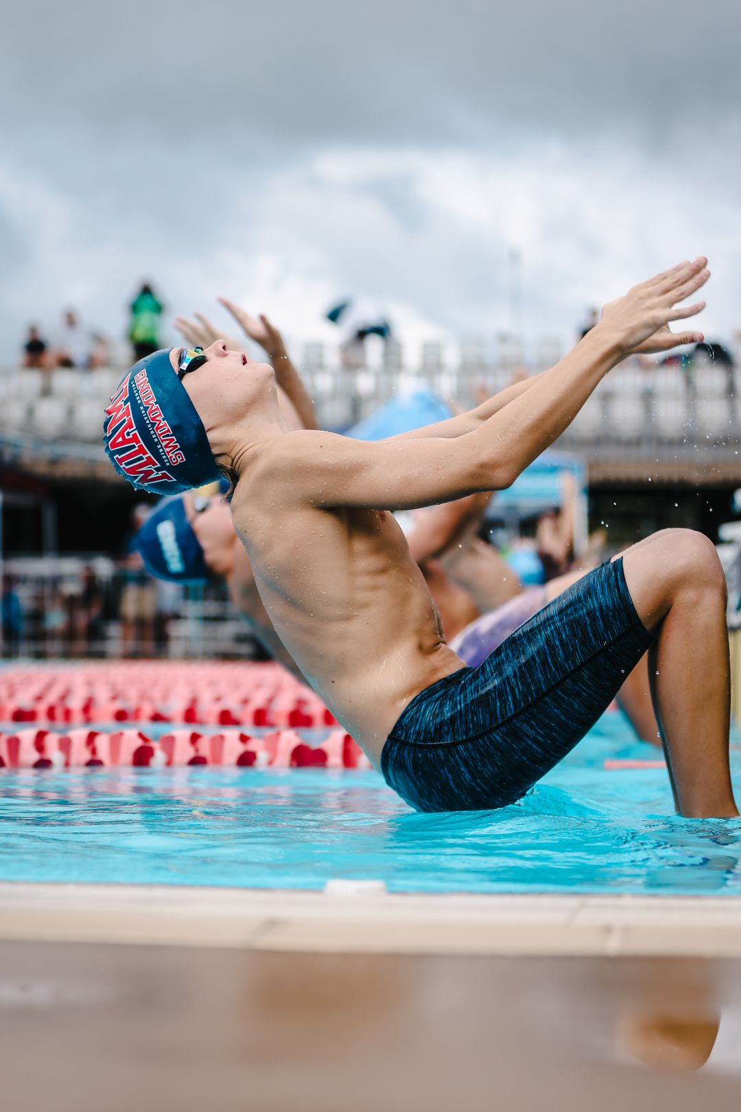 Swimmer in blue cap performing dramatic pool entry during competition.