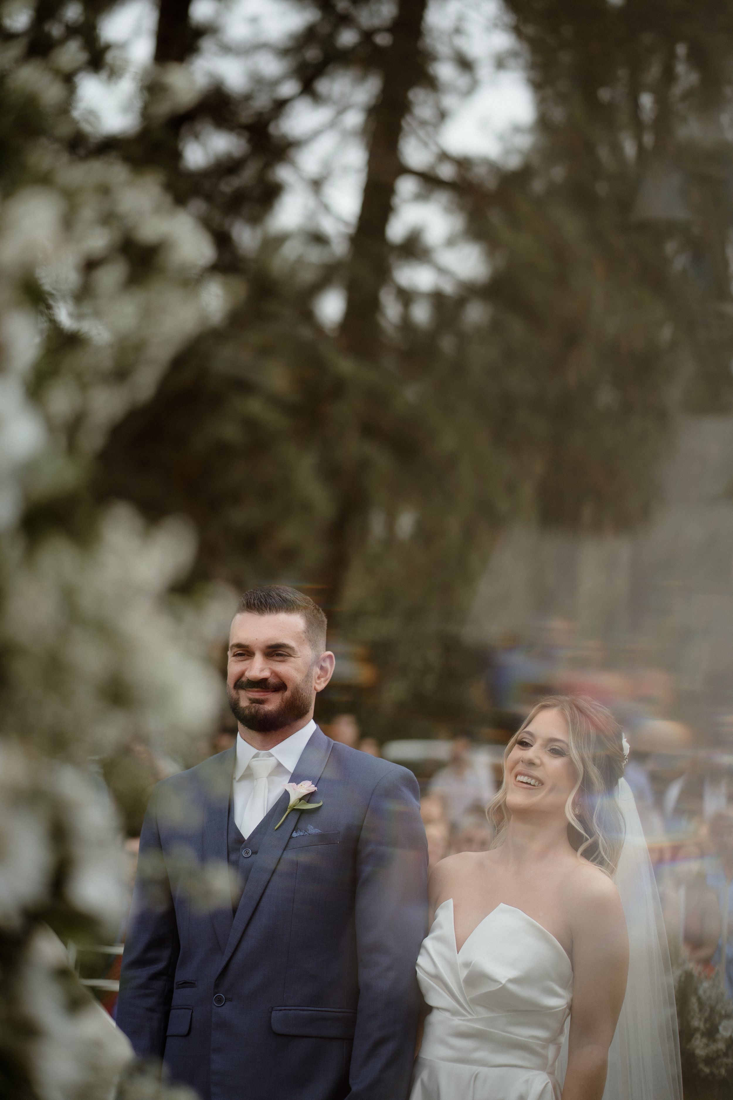 Couple shares emotional moment during wedding ceremony under trees with soft lighting.