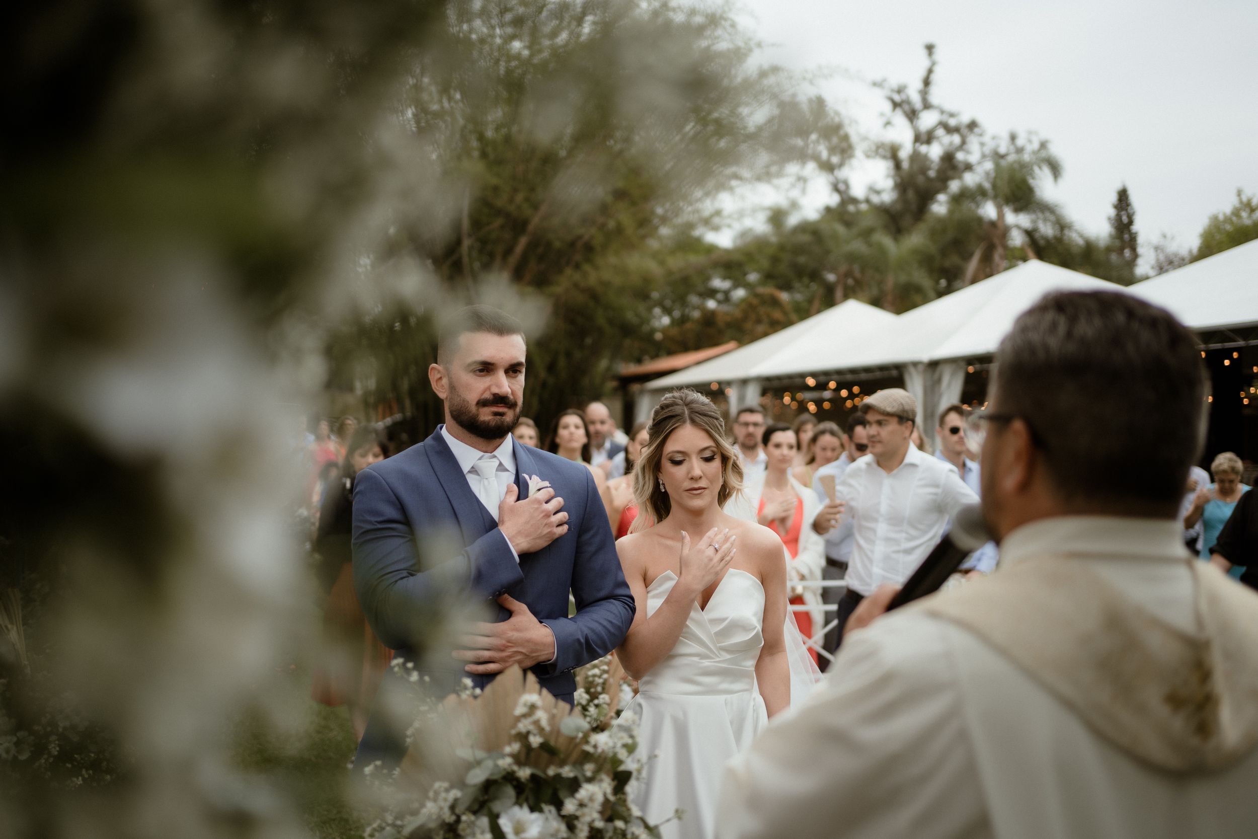 Wedding guests clap and celebrate during an outdoor ceremony under natural greenery.