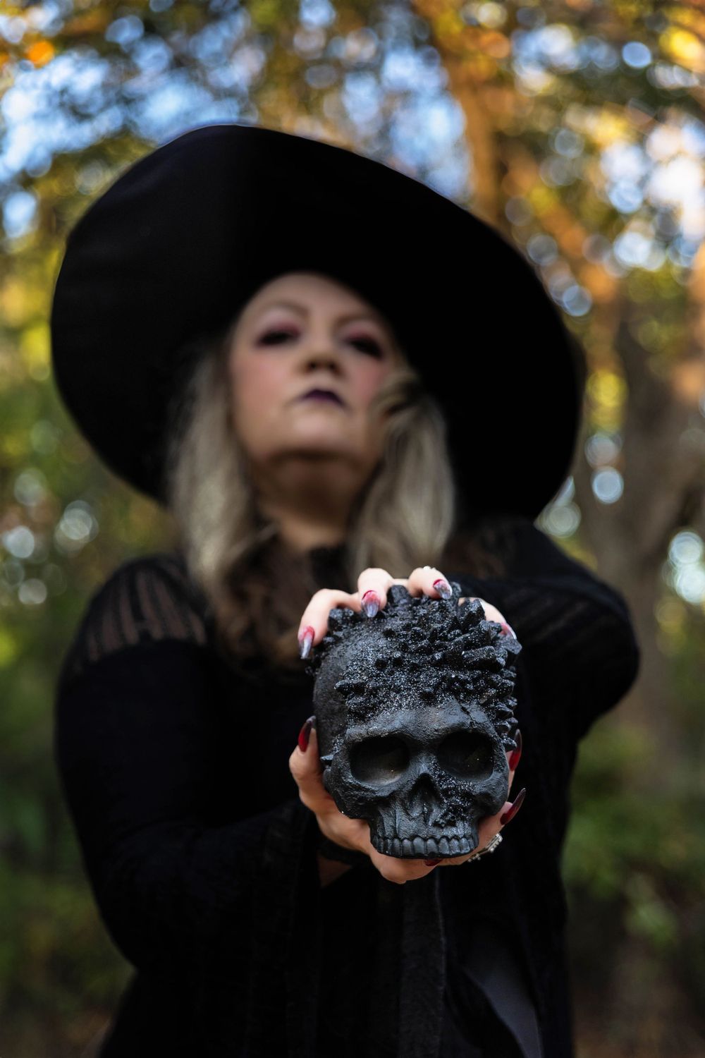 A beautiful witch in the woods. She holds a black skull.
