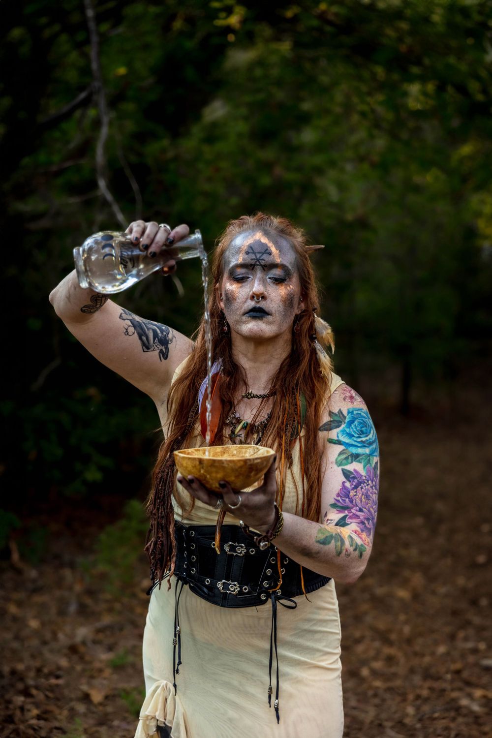 a bohemian witch pours water into the top of a skull.
