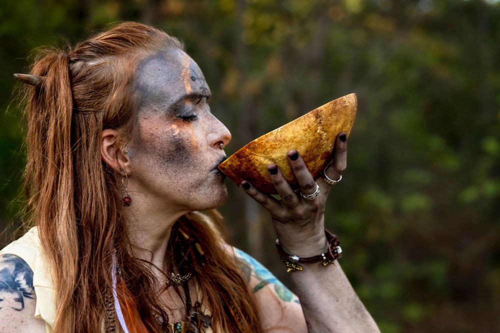 A bohemian witch drinks from the top of a skull.