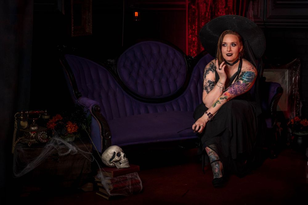 A woman sits in a spooky studio setting a poses for the camera.