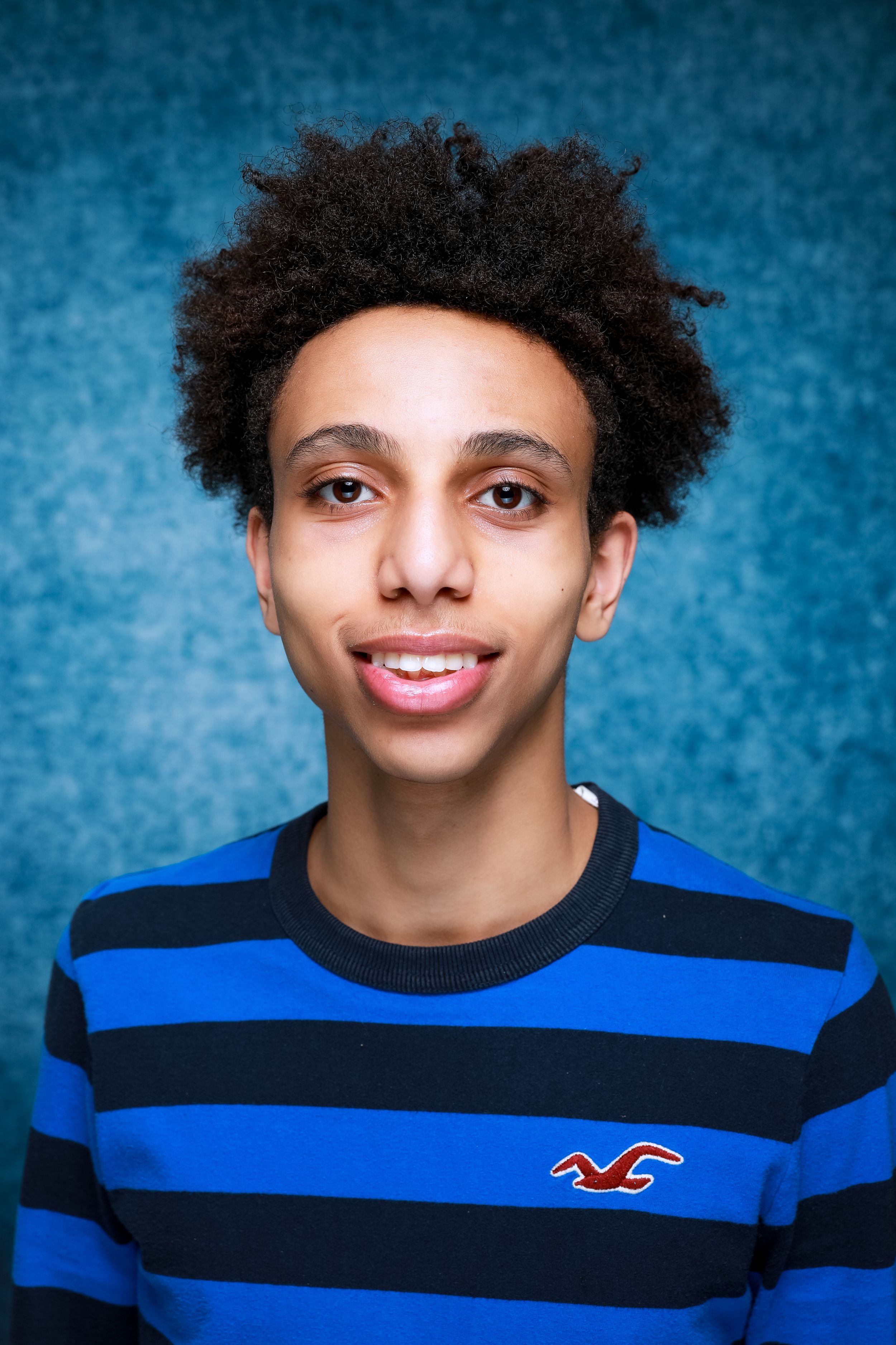 Portrait of teen in blue and black striped shirt against blue background.