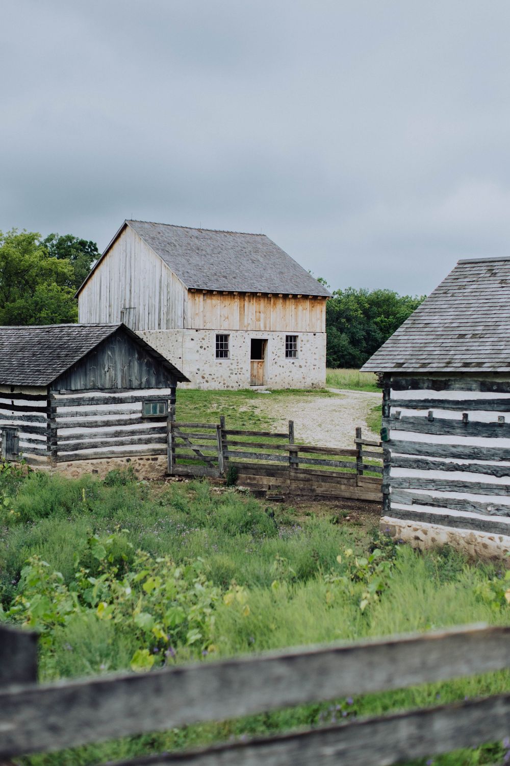 Rustic wooden barns and fences on a rural property with green grass and wildflowers.