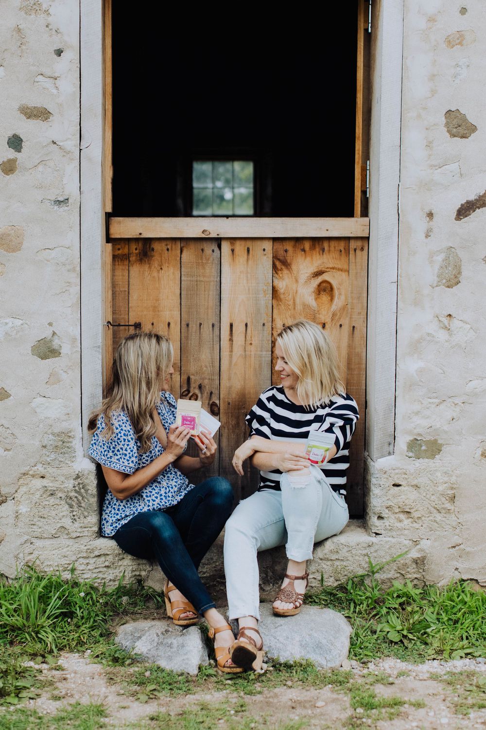 Friends lounging and laughing together against rustic barn wall.