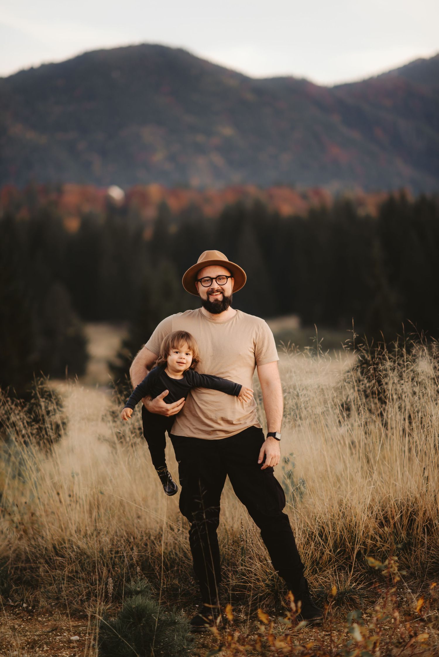 A heartwarming autumn portrait in a golden mountain meadow with tall dry grass and evergreen trees.