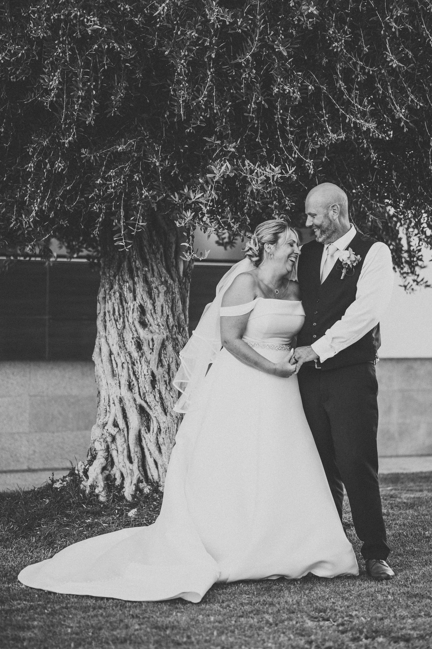 A black and white wedding portrait under a weeping willow tree on a lawn.
