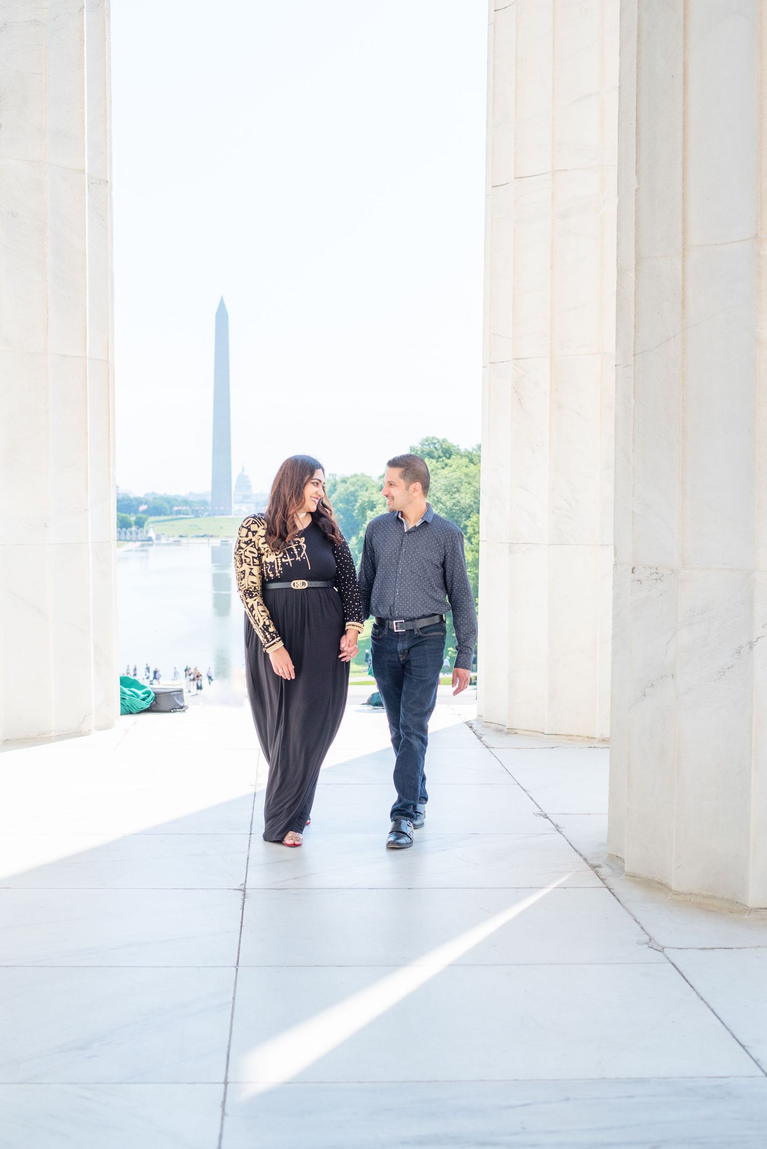 husband and wife look at each other on walk by Lincoln Memorial, Washington Monument in the background