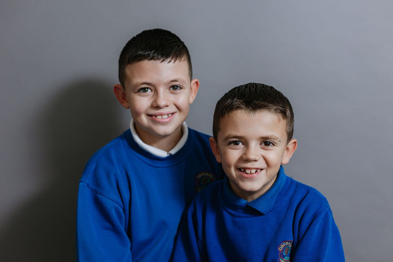Two boys wearing matching blue school uniforms pose for a portrait photo.