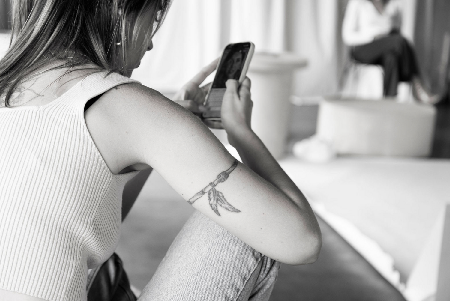 Black and white photo of person using smartphone while sitting on bed.