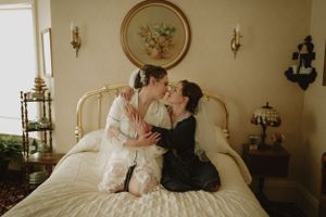 Two people sharing an intimate moment on an antique bed in a vintage-styled room.