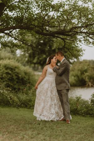A tender wedding moment captured between newlyweds under a green tree canopy.