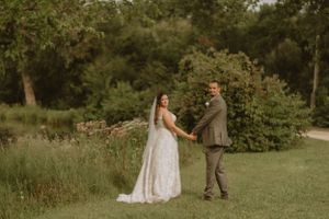 A wedding couple holds hands while standing in a lush green garden setting.