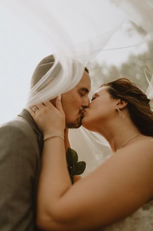 A romantic wedding kiss moment captured in warm sunlight with the bride's veil flowing softly in the breeze.