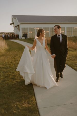 A couple strolls along a pathway outside a modern white chapel at dusk.