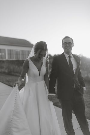 A couple walks together in elegant wedding attire during golden hour.