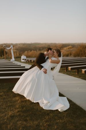 Two people in wedding dresses share a romantic dip pose at sunset.