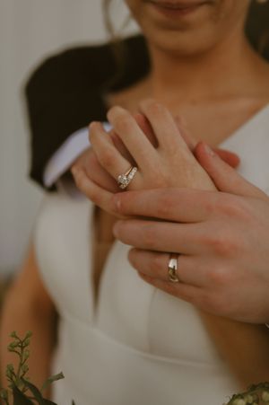 Close-up of hands showing wedding and engagement rings against a white dress.