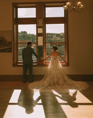 A wedding couple silhouetted against large windows with sunlight casting dramatic shadows on the floor.