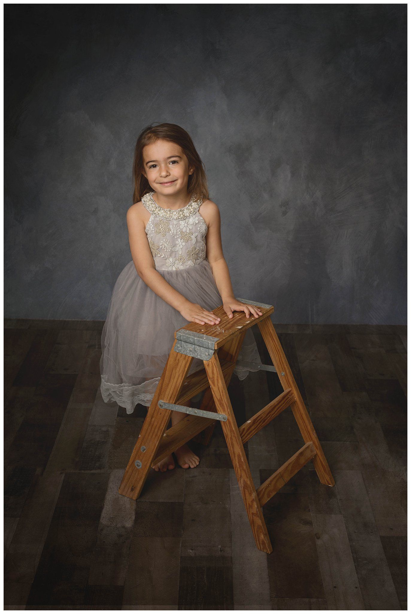 Child standing on wooden ladder stool in studio portrait session with dark backdrop photographed by Austin children photographer